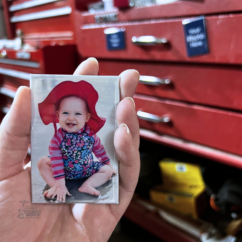 Custom baby photo toolbox magnet featuring a smiling baby in a red sun hat held in hand in front of a red mechanic toolbox background.