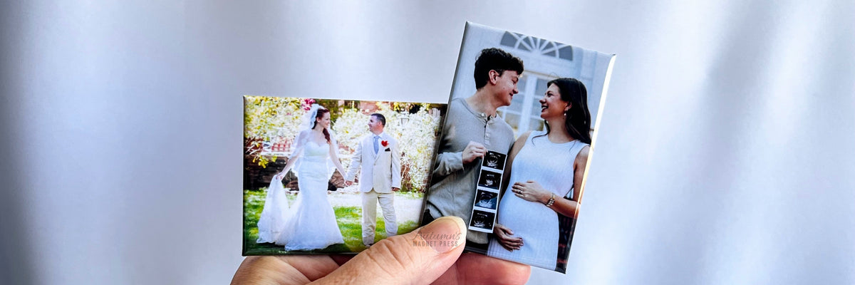 A hand holding two small printed photographs against a soft white draped fabric background. One photo shows a bride and groom outdoors, and the other shows a pregnant woman in a white dress holding a baby monitor.