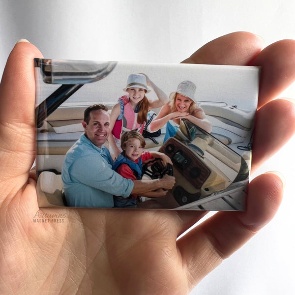 Hand holding a custom family photo magnet featuring a family enjoying a day together on a boat against a soft white background.
