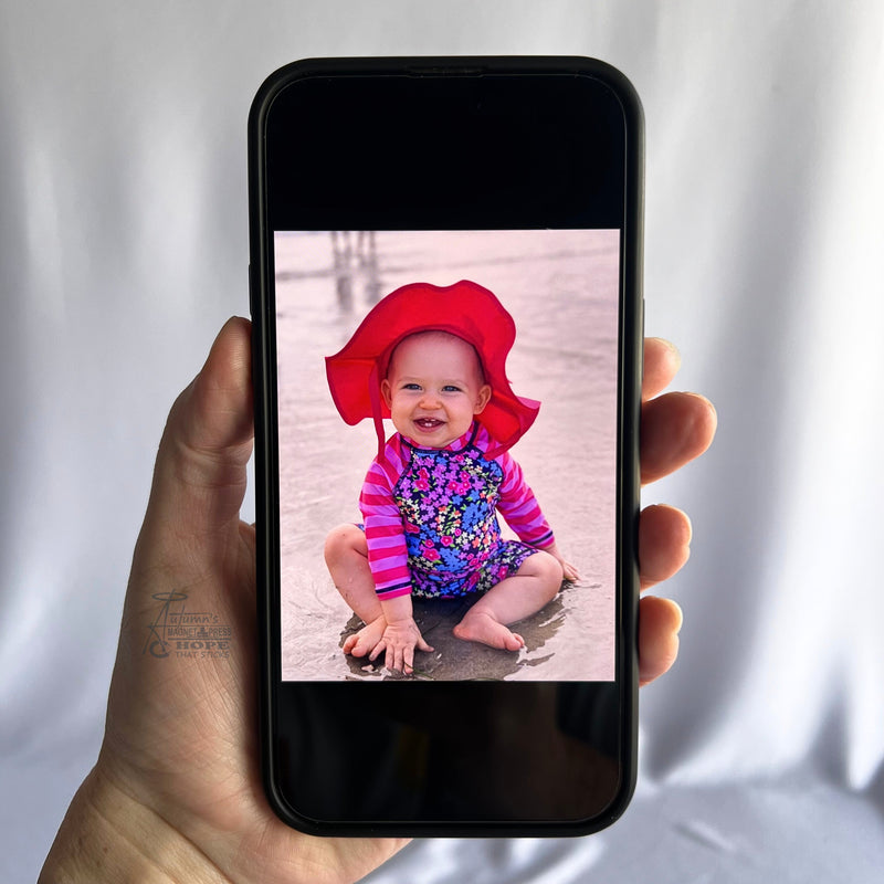 Hand holding a smartphone displaying a baby beach photo used to create a custom photo magnet design.