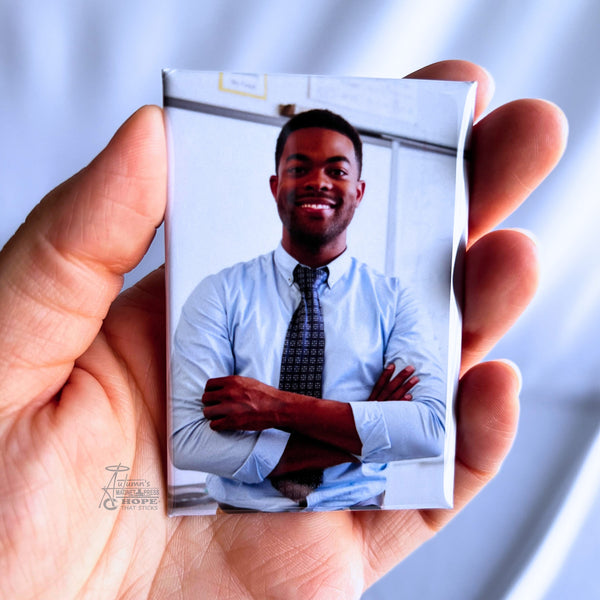 Hand holding a custom teacher portrait photo magnet featuring a smiling teacher standing in a classroom against a soft white background