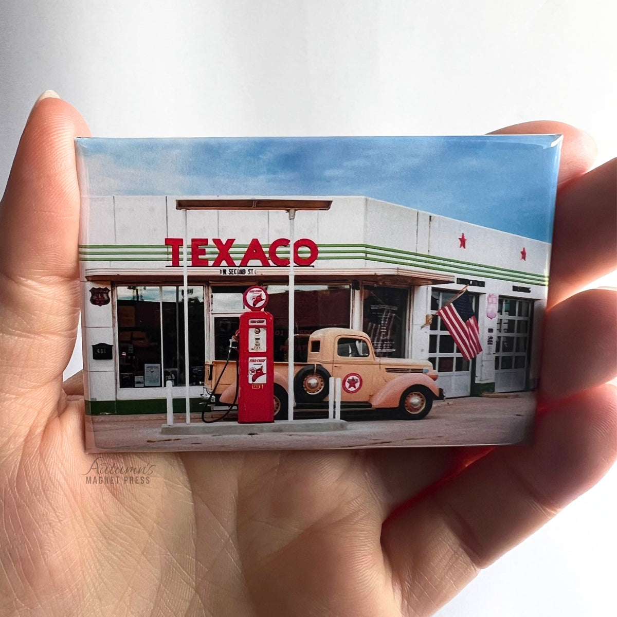 Hand holding a custom photo magnet featuring a vintage Texaco gas station building against a soft white background.