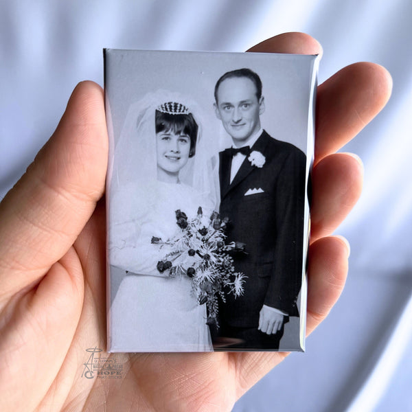 Hand holding a custom vintage wedding photo magnet featuring a black and white portrait of a bride and groom against a soft white background